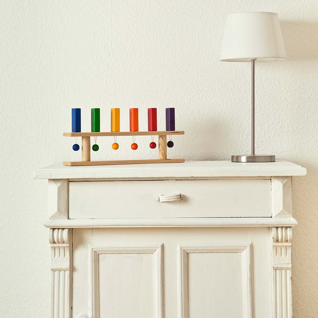 Buntes Standdomino von FRIDLIN mit 6 farbigen Steinen in Regenbogenreihenfolge, dekorativ platziert auf einer weißen Kommode.